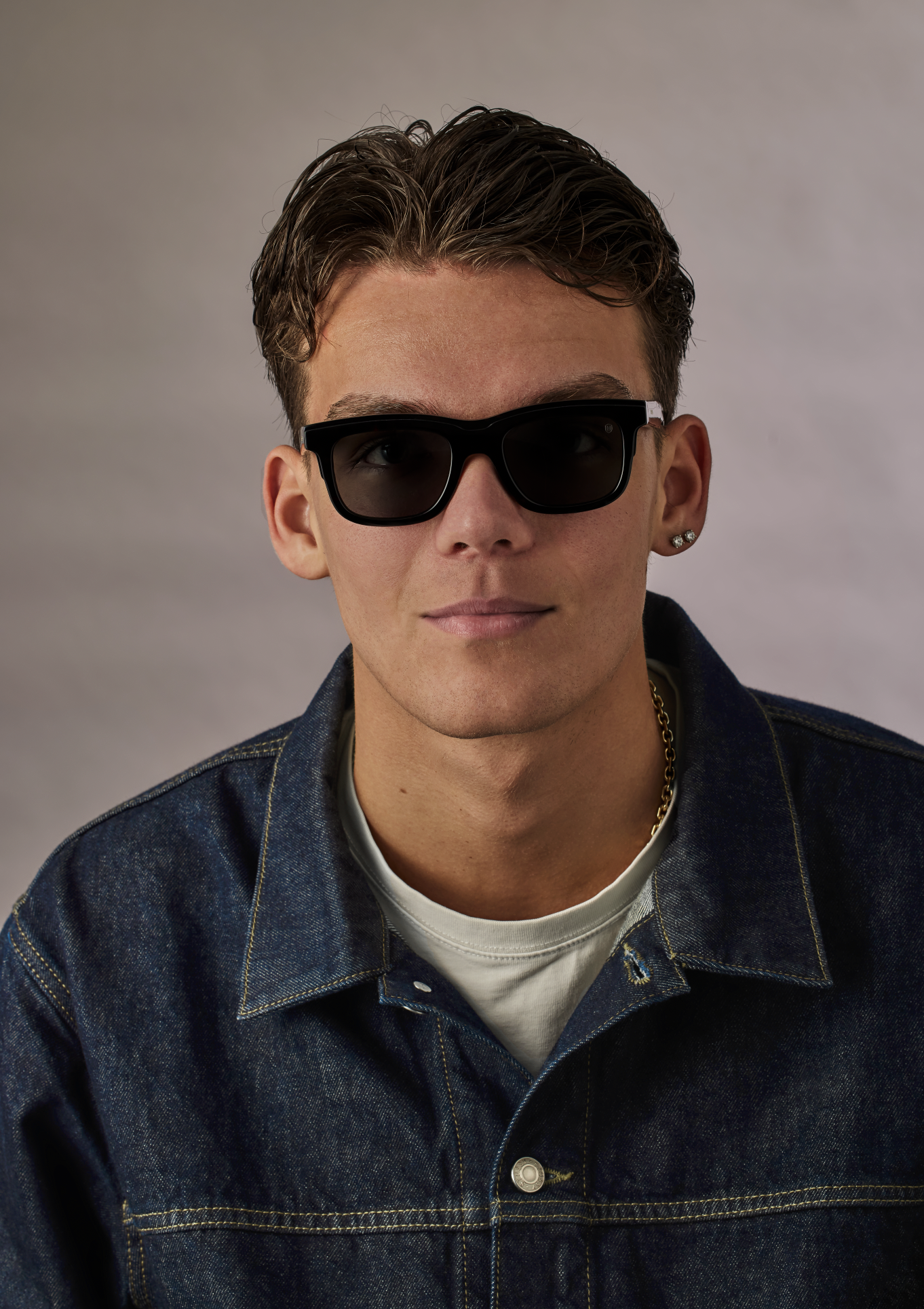 Person wearing sunglasses and a denim jacket against a neutral background