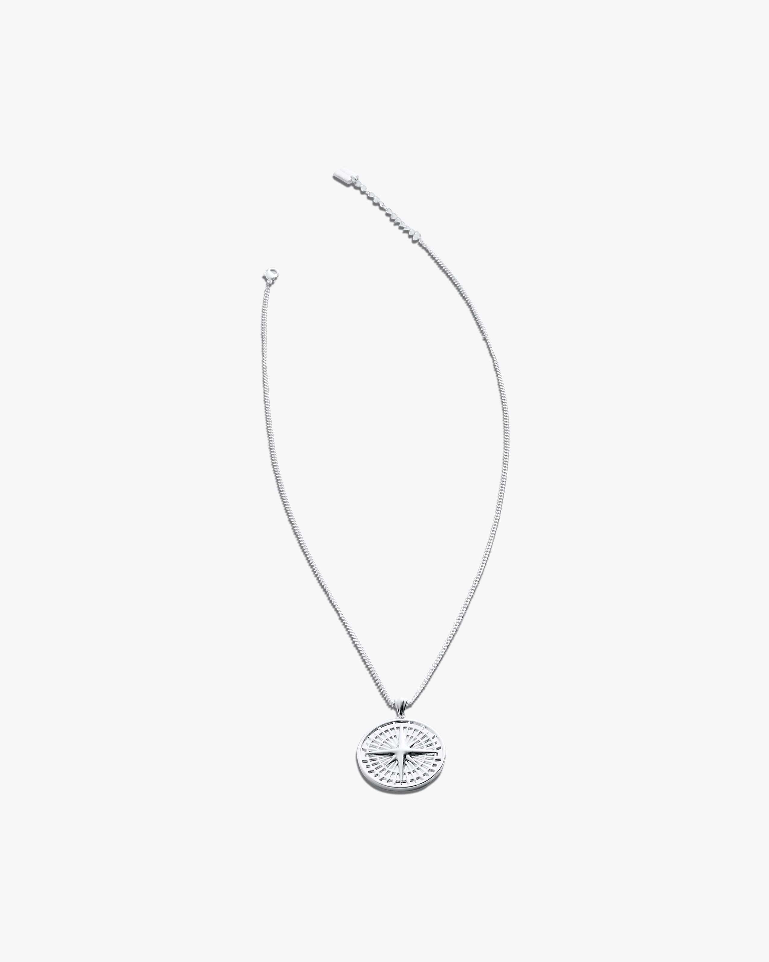 Silver necklace with a compass pendant on a light grey background