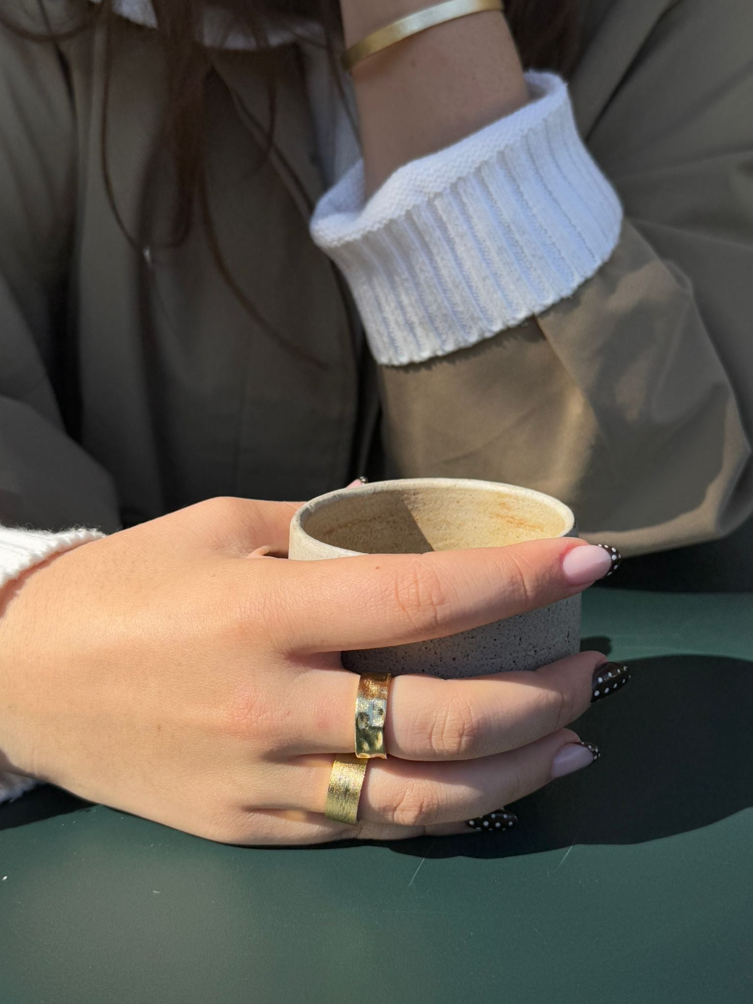 Hand holding a small cup with a focus on the fingers and nail polish.