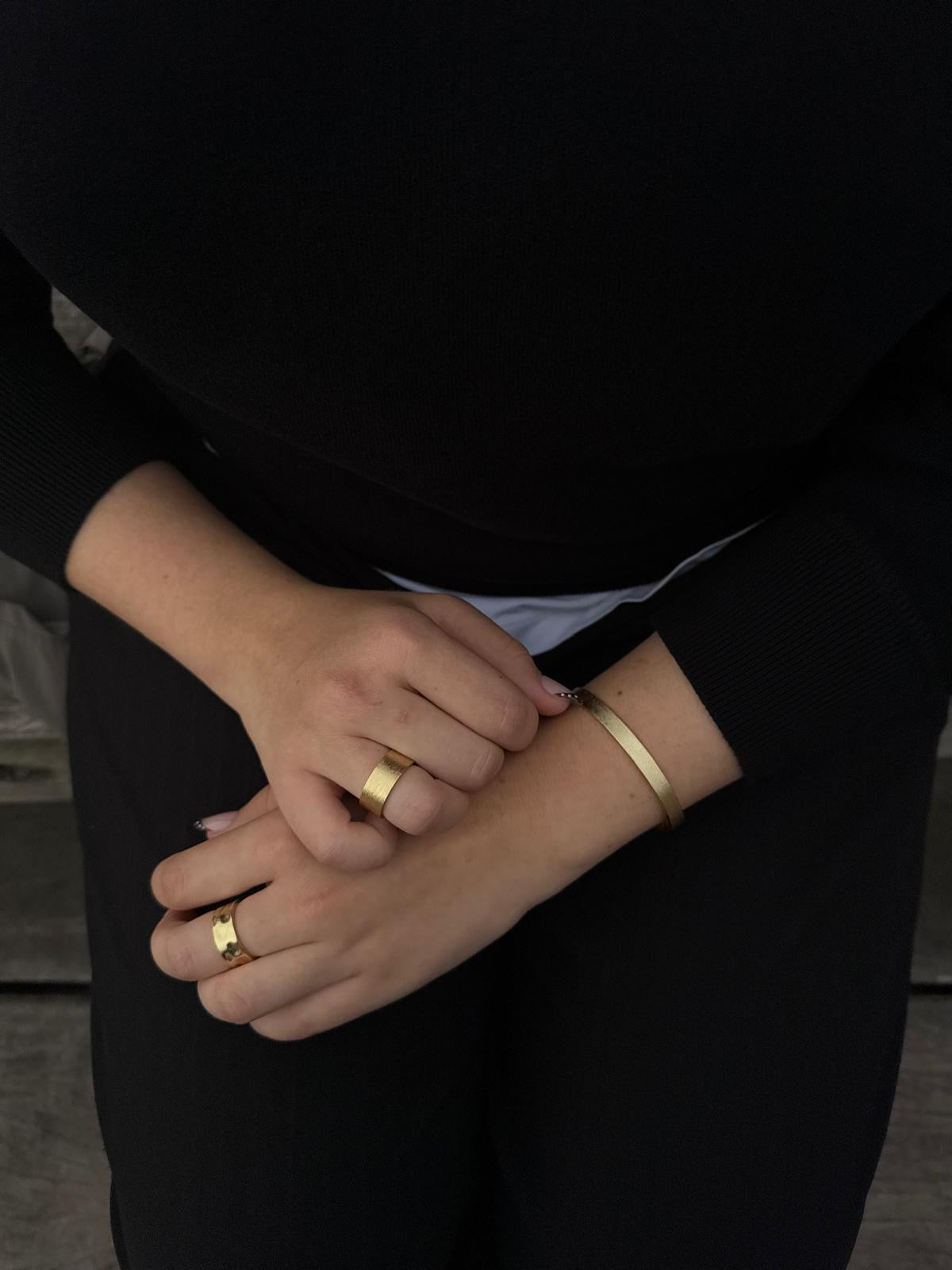 Close-up of hands wearing gold rings and a bracelet against a dark background