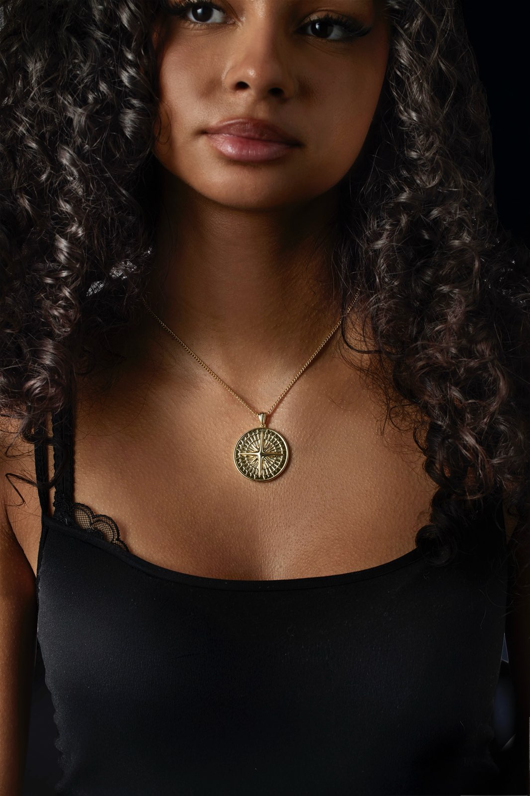 Woman wearing a necklace with a circular pendant against a dark background