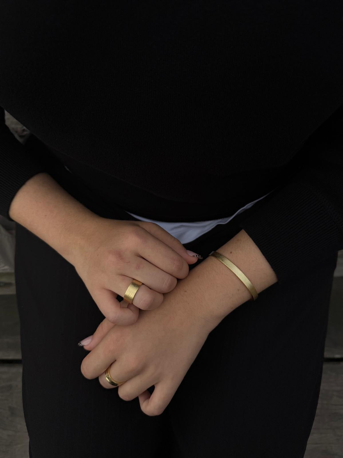 Close-up of a person wearing gold rings and a bracelet on a black background