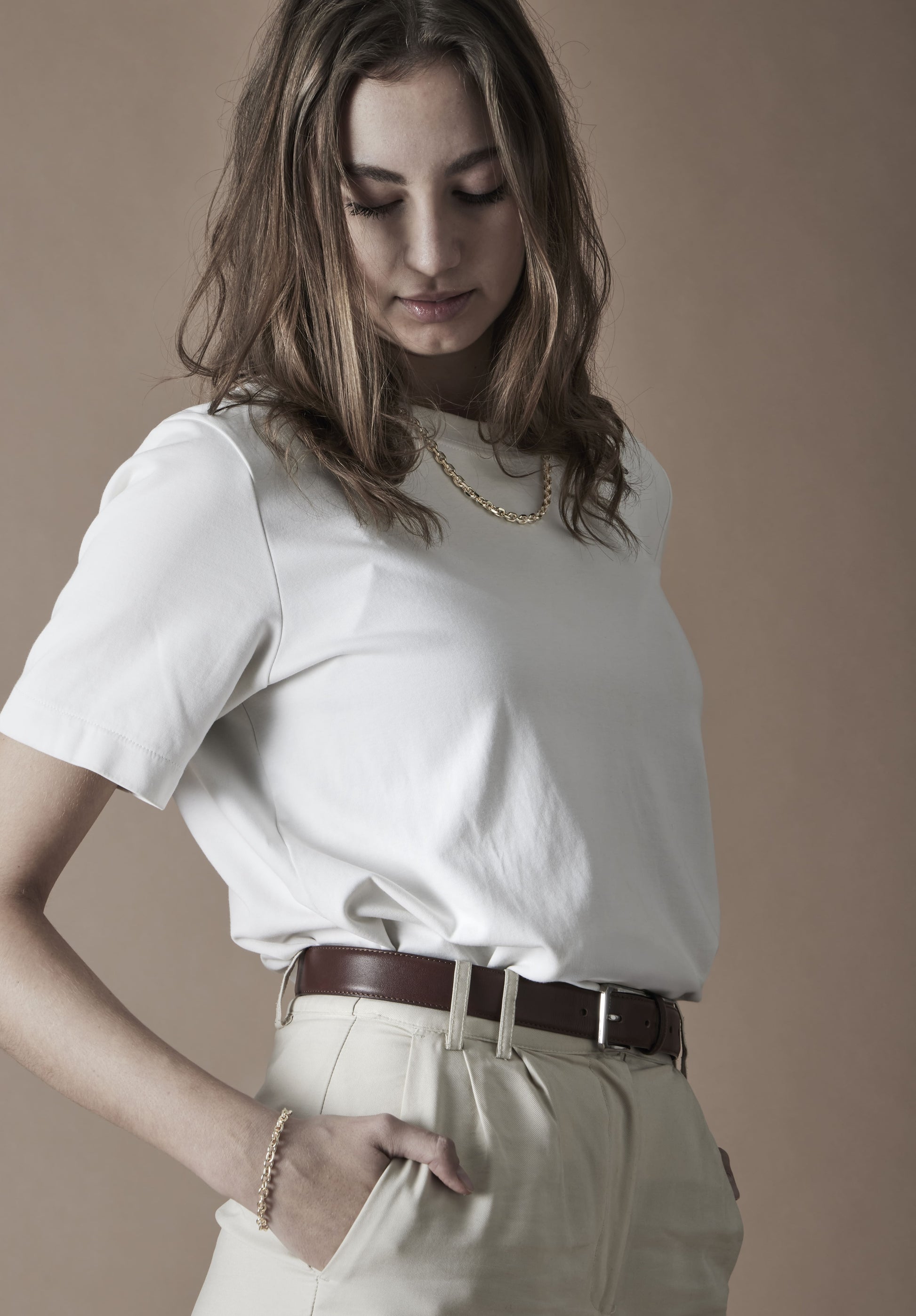 Woman wearing a white t-shirt and beige pants against a plain background