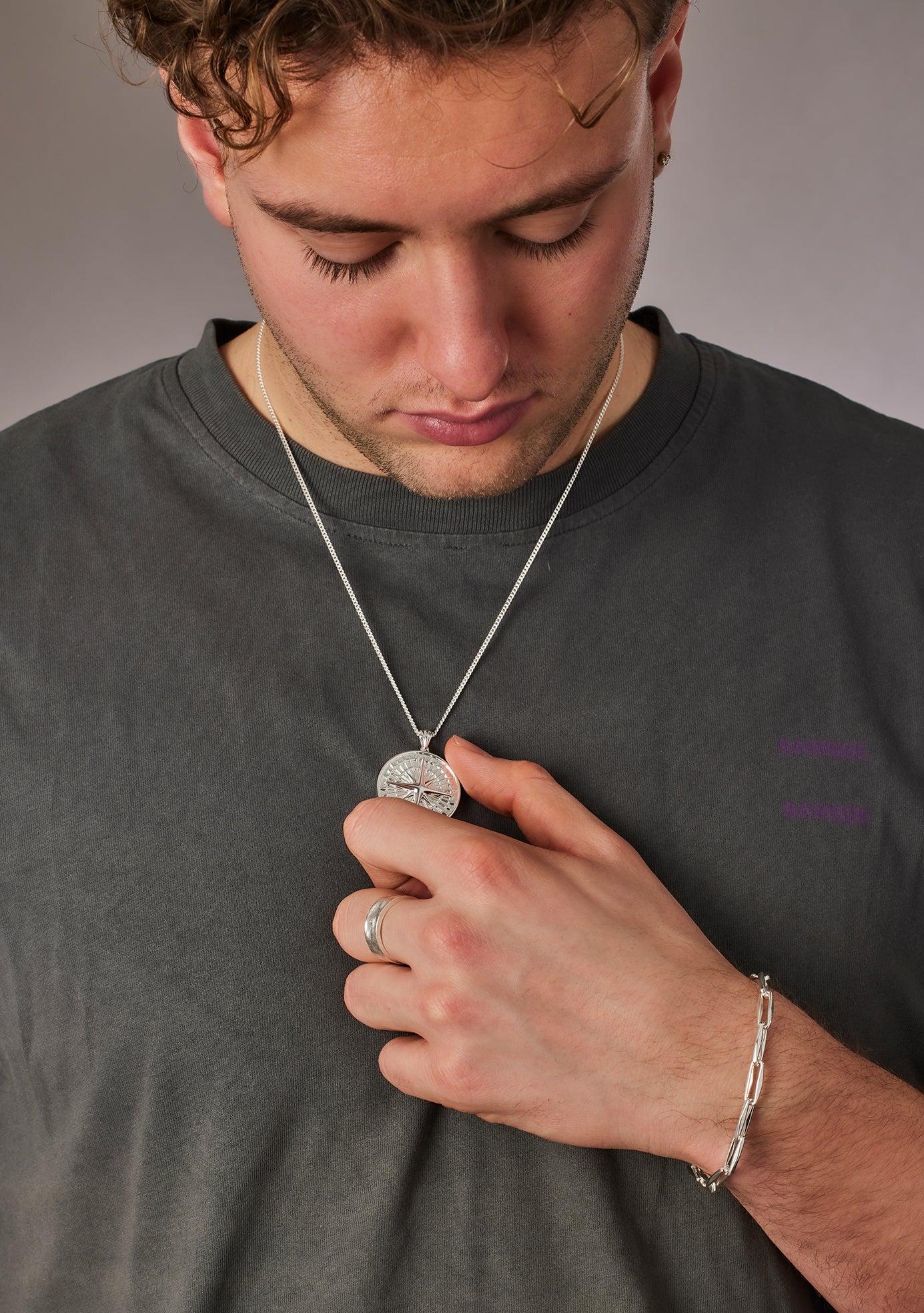 Man wearing a necklace with a pendant, holding it with his hand against a gray background