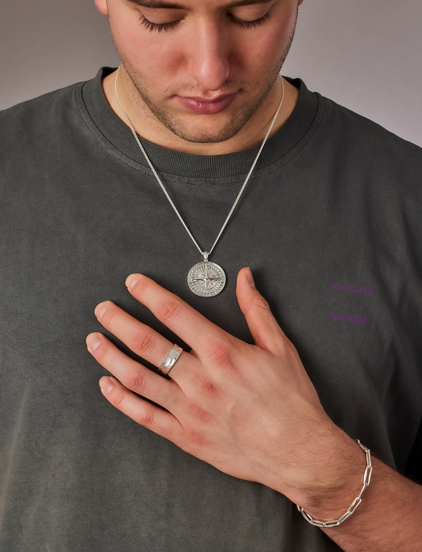 Man wearing a necklace, ring, and bracelet on a plain background