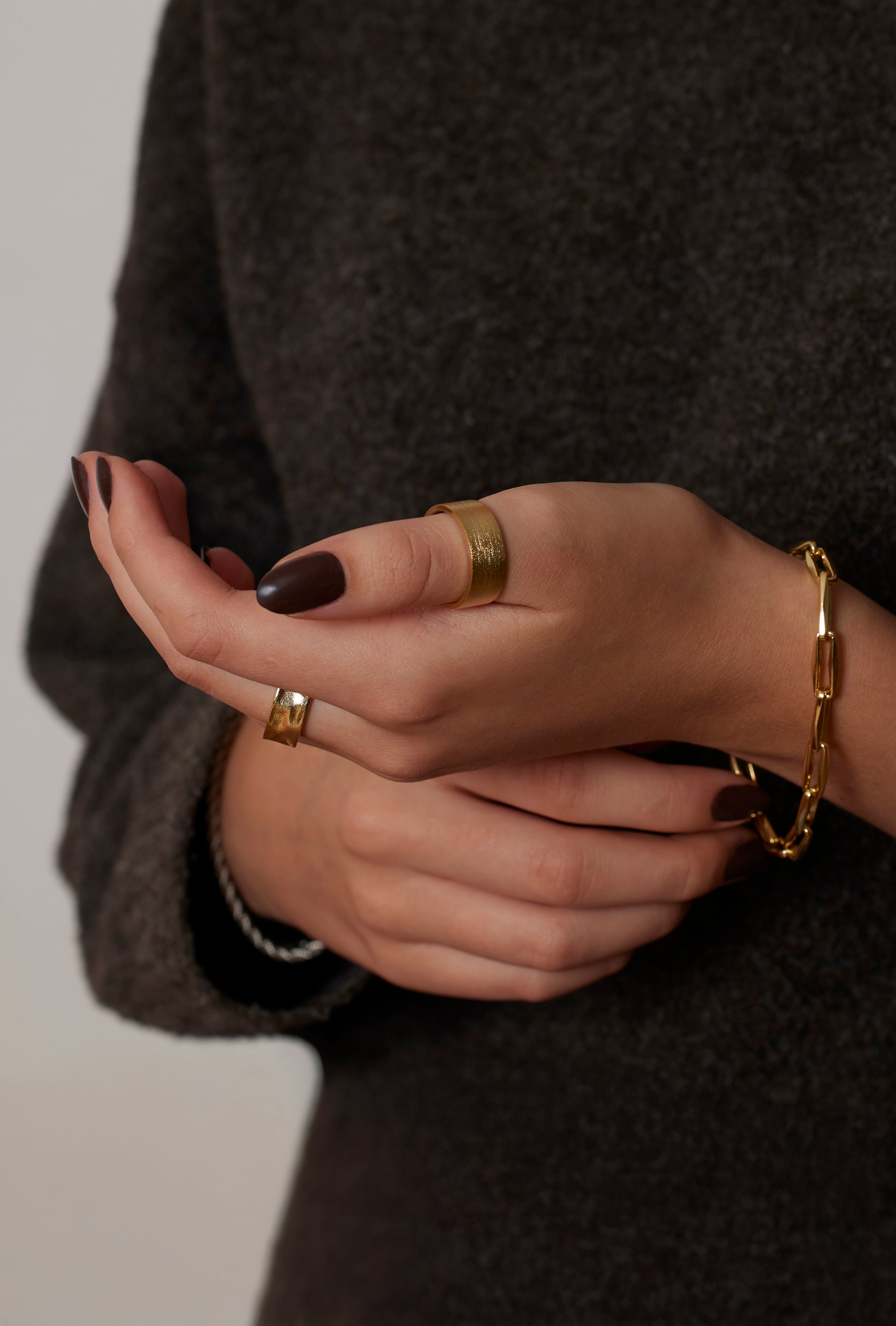 Close-up of hands with gold rings and bracelets against a dark background