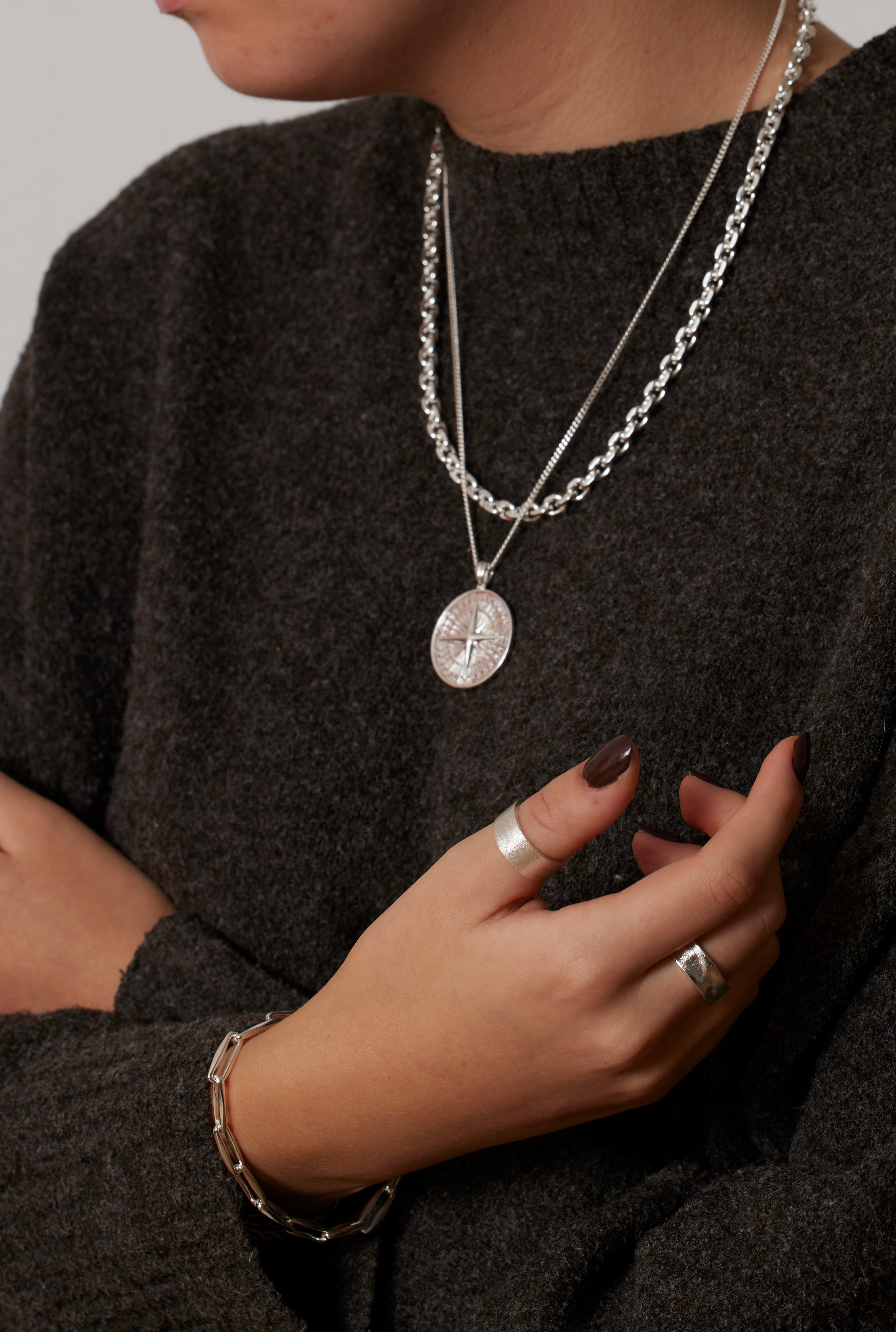 Woman wearing a dark sweater with layered silver necklaces and rings.