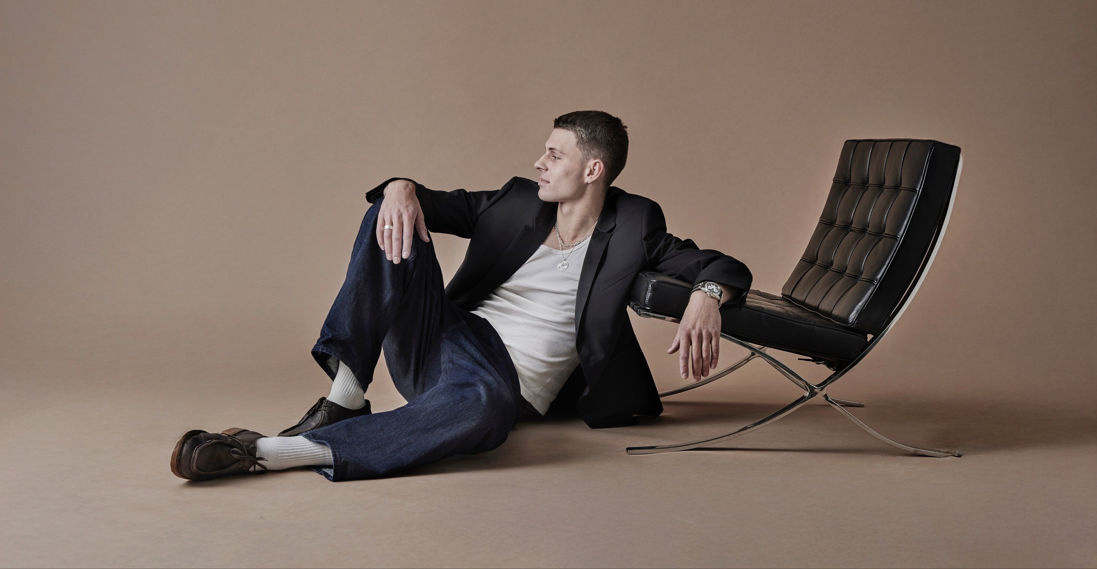Man in a suit sitting on the floor next to a modern chair against a beige background
