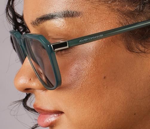 Close-up of a person wearing green eyeglasses with 'Hobbs' branding.