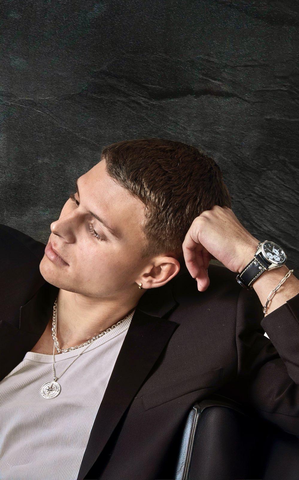 Man in a suit with a watch and jewelry against a dark background