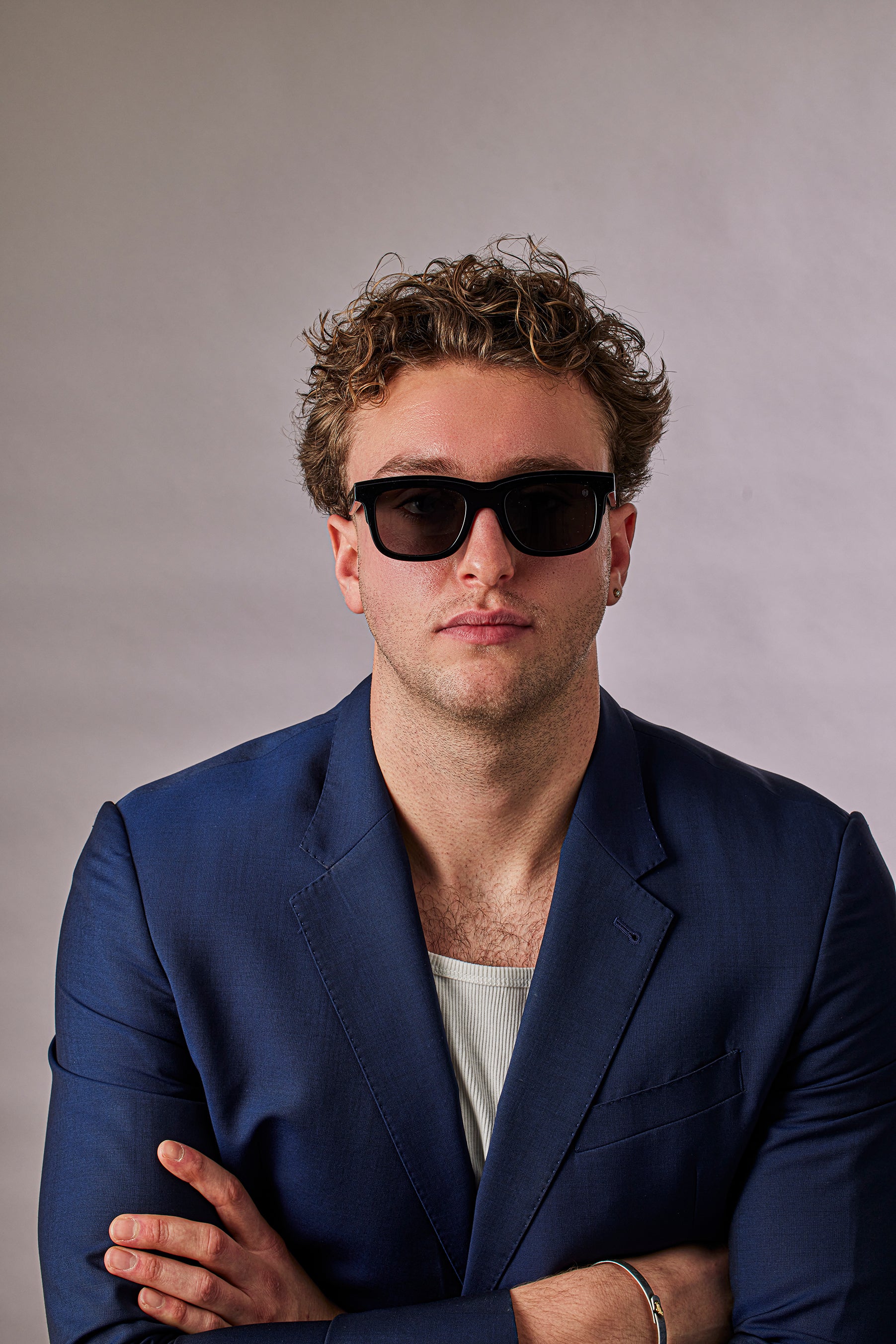Man wearing sunglasses and a blue blazer against a plain background