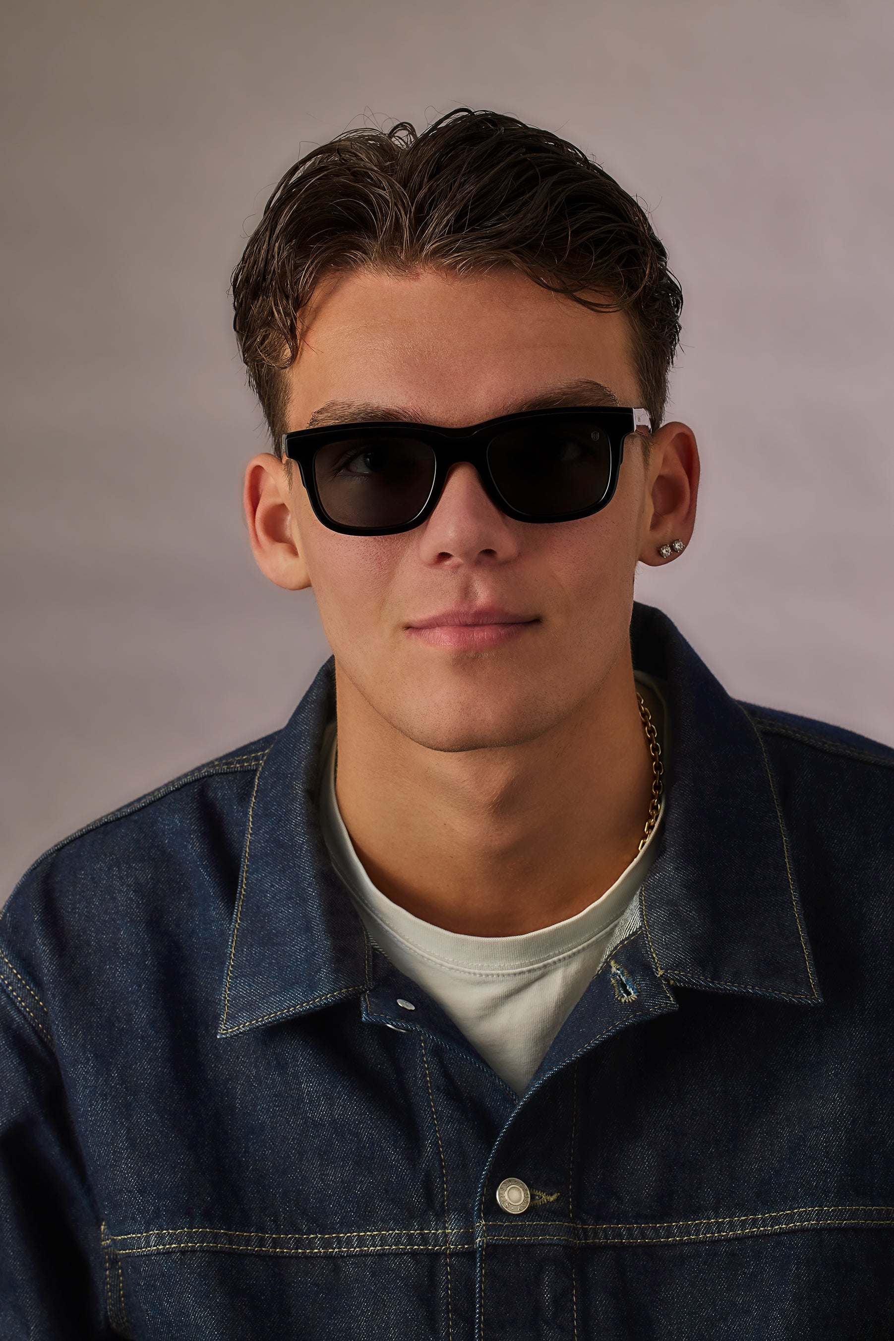 Man wearing sunglasses and a denim jacket against a plain background