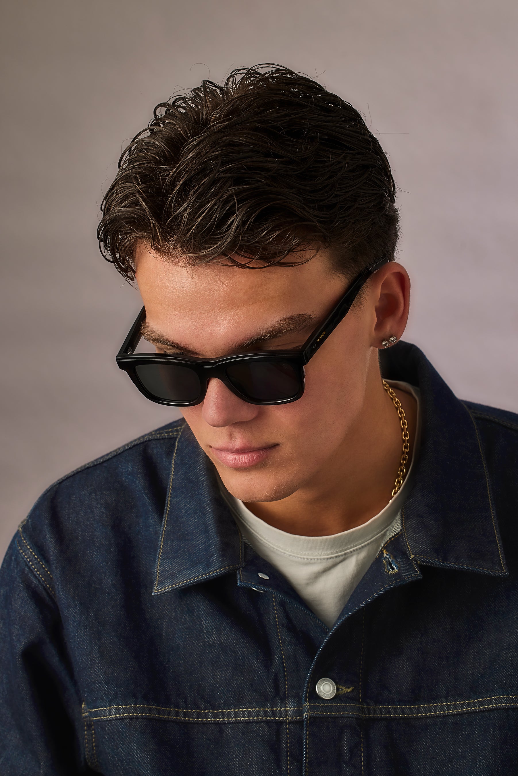 Man wearing sunglasses and a denim jacket against a plain background
