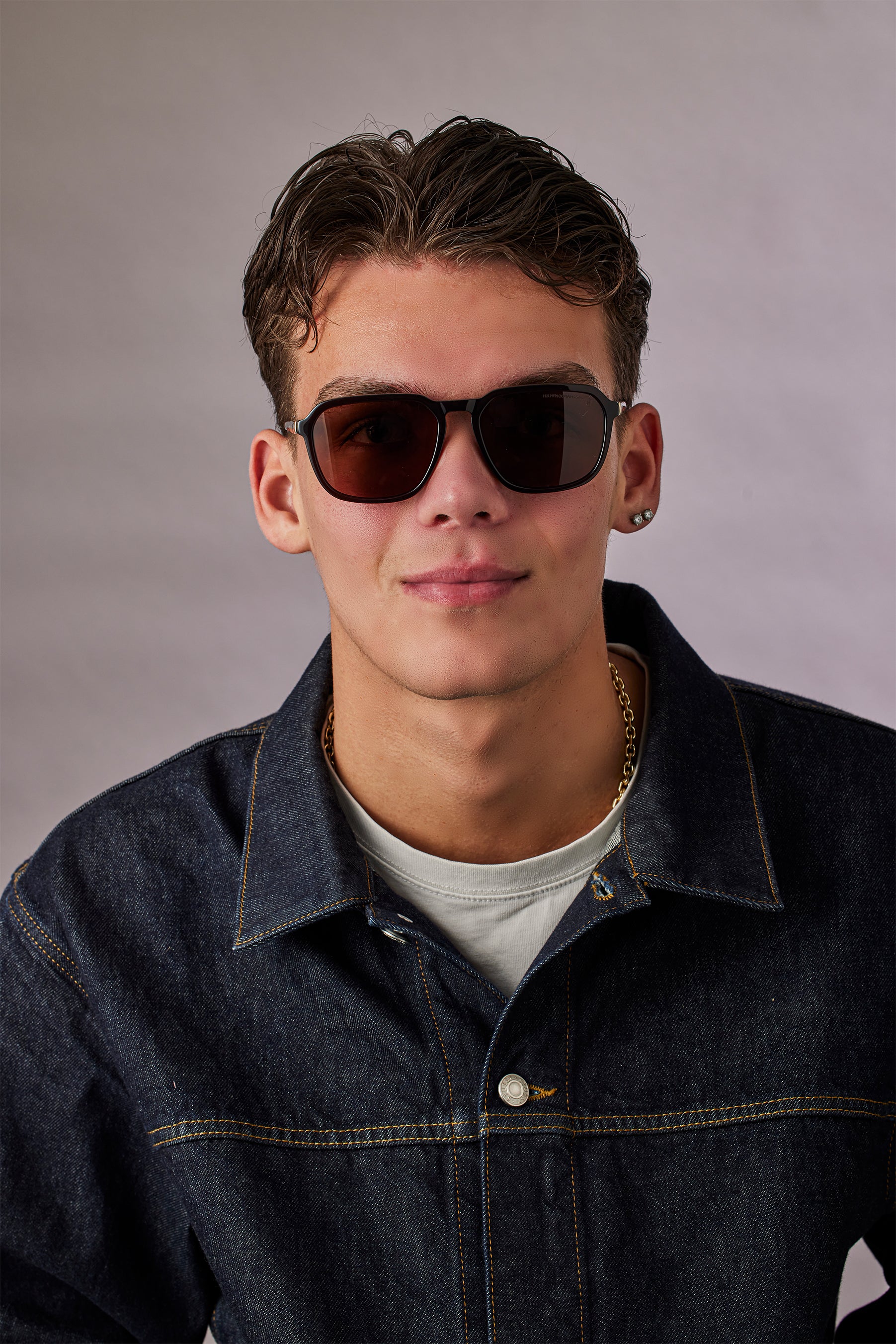 Person wearing sunglasses and a denim jacket against a plain background