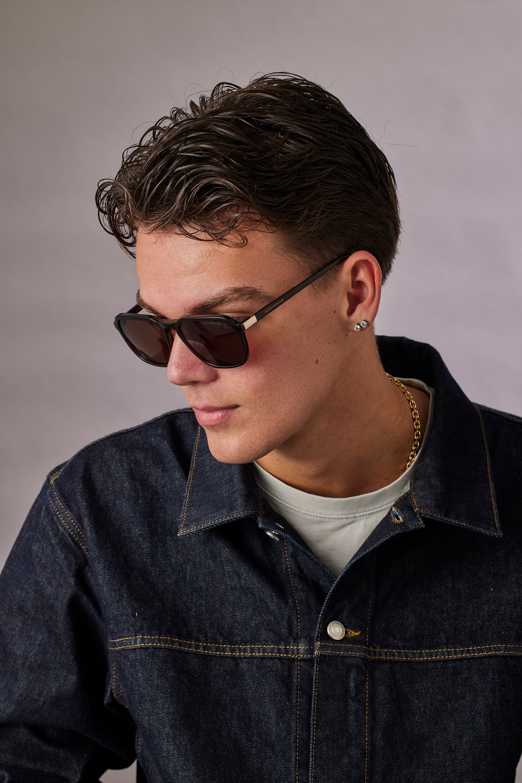 Man wearing sunglasses and a denim jacket against a gray background