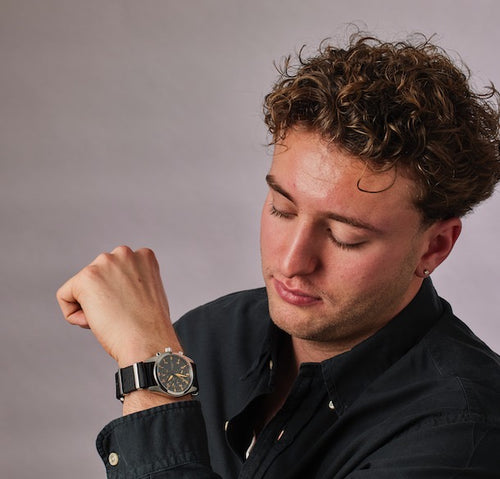 Man wearing a black watch on his wrist against a gray background